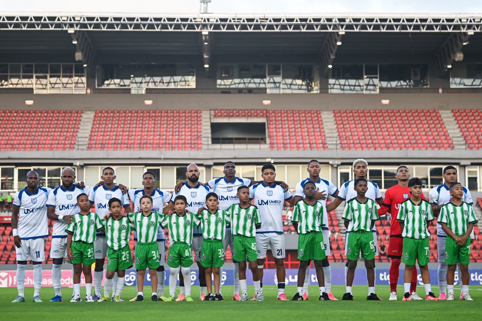 Plantilla de UMECIT FC junto a niños acompañantes antes del partido frente a Alianza FC